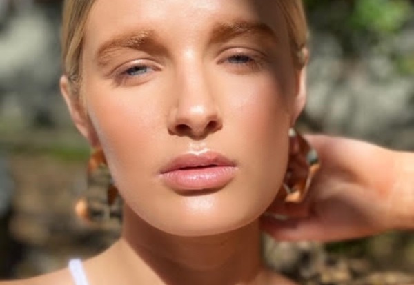 Natural nude makeup on blonde woman with gold earrings in shady forest location.